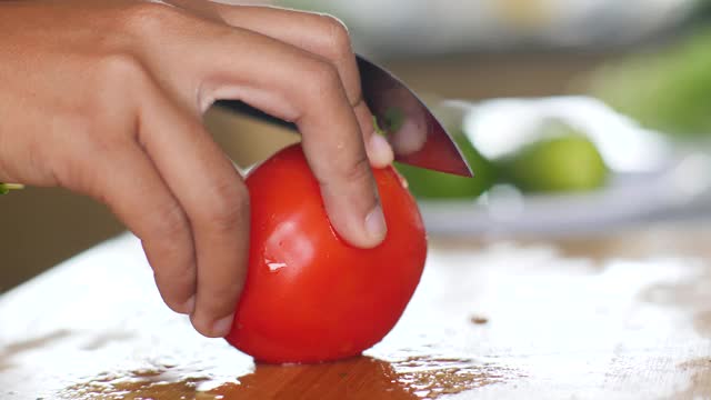 微距镜头，一个女人的手在木砧板上切一个成熟的番茄。视频素材