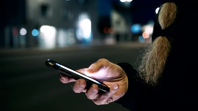 一个长着胡子的陌生男子晚上在人行道上使用智能手机，社交媒体会提示你点赞、评论和关注者视频下载