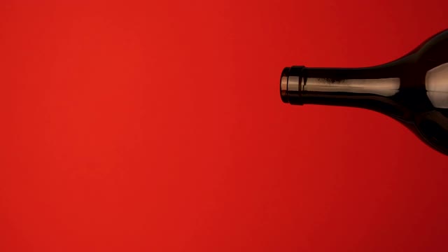 一个酒瓶的颈部的特写，红酒从里面倒出来。红酒从红色背景的暗色玻璃瓶中倒出。葡萄酒从瓶中反向流出视频下载