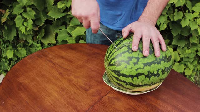 一名男子在盘子上切下一片西瓜。视频素材