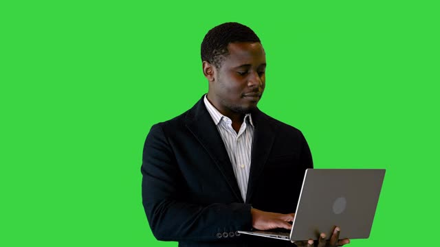 英俊的非裔美国商人站在电脑前工作在绿屏上，色度键视频素材