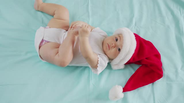 有趣的小婴儿笑了2021年。可爱的小男孩戴着圣诞老人的帽子躺在沙发上。视频下载