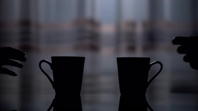 两个陶瓷杯的黑色轮廓，一个男人和一个女人的手从桌子上拿起它们视频素材