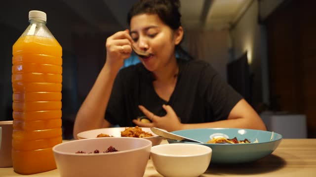 亚洲妇女在家里喝橙汁吃晚餐。视频素材