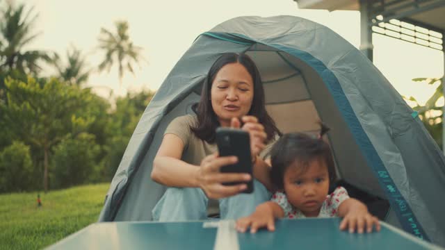 快乐的女人带着带着智能手机的姐姐在家里的帐篷里微笑视频素材
