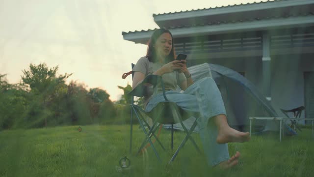 拿着智能手机微笑的快乐女人坐在前面的花园里视频素材