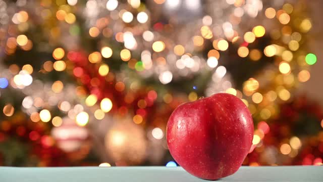 一个人用手拿苹果。背景是一棵装饰着花环的圣诞树。镜头的运动。视频下载