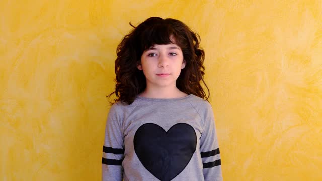11岁的卷发女孩在黄色的墙上摆姿势。快乐女孩的肖像在相机微笑。4 k视频素材