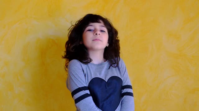 11岁的卷发女孩在黄色的墙上摆姿势。快乐女孩的肖像在相机微笑。4 k视频素材