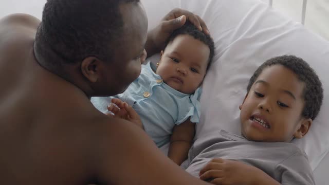 非洲父亲与两个3个月大的孩子和3岁大的孩子一起呆在家里，预防冠状病毒或Covid-19疫情的幸福家庭。家人时刻的概念。视频素材