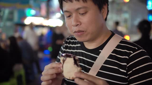 一名亚洲男子在泰国曼谷街头吃巧克力吐司。视频素材