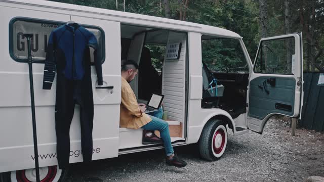 一名日本冲浪者在他的迷你面包车里的公路旅行中用笔记本电脑工作视频下载