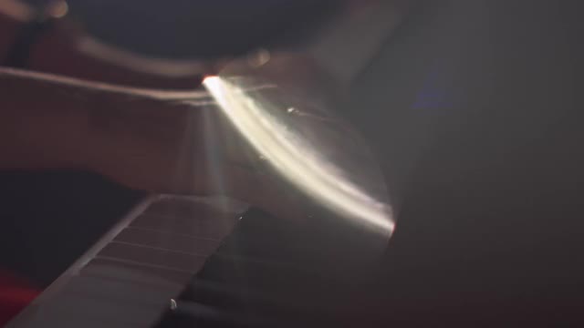 一位女钢琴家在一架漂亮的大钢琴上弹奏着轻柔的古典音乐，特写慢动作。钢琴琴键用深色拉近。前景中来自光线和烟雾的眩光视频素材