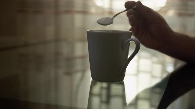 一个男人用勺子把糖倒进一个杯子里，背景是一扇明亮的窗户视频下载