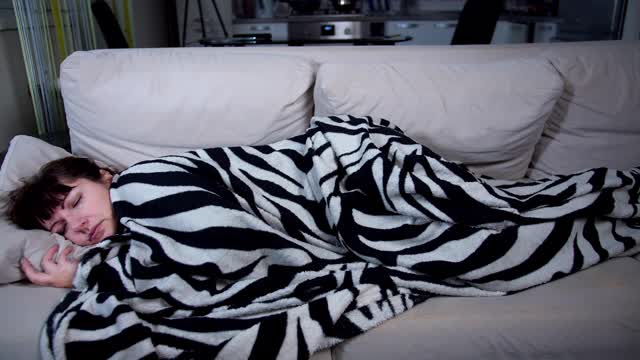 疲惫的女人躺在沙发上，盖着毯子睡在家里视频素材