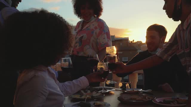 年轻的多种族朋友在开胃菜和日落的时候，戴着保护面罩，用红酒杯敬酒视频下载