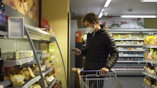 一个戴着面具在杂货店看手机的男人视频素材