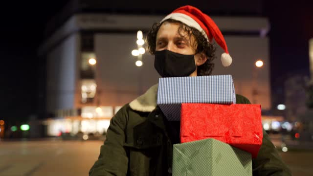 一名戴着防护口罩的男子手持礼盒在购物中心，在新冠肺炎疫情下购物，感恩节和圣诞节概念。视频下载