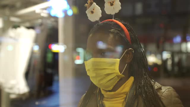 一个戴着面罩的女人透过商店橱窗看圣诞礼物的概念视频下载
