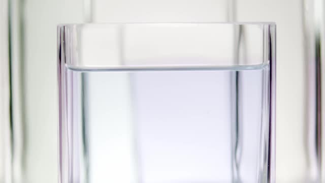 一片柠檬在白色背景下落入玻璃容器中的水中视频素材
