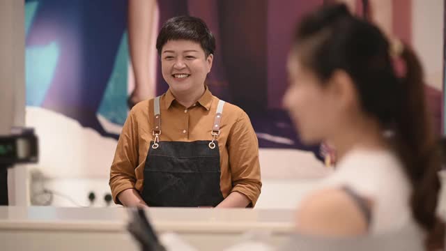 亚洲华人服装店收银员在柜台与她的顾客交谈视频下载