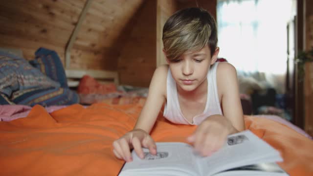 一个有趣的少年躺在床上，在室内看书视频下载