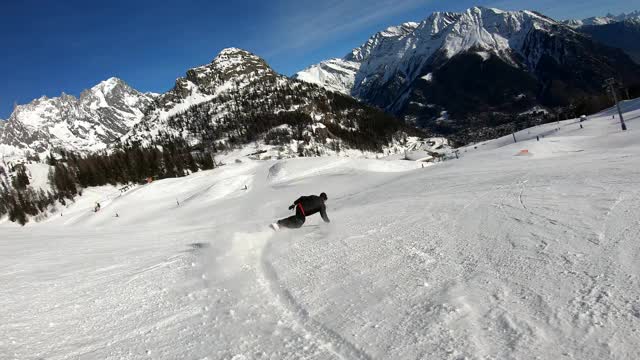 在Courmayeur滑雪胜地，一名专业滑雪板骑手的4K超高清慢镜头，滑雪板上快速雕刻着满是积雪的勃朗峰(Mont Blanc)，背景被阿尔卑斯山蓝天上的太阳照亮视频下载