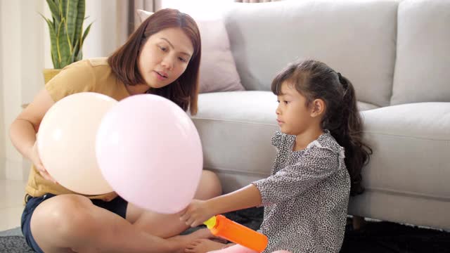 妈妈和可爱的小女孩在家里客厅的沙发上玩气球视频下载