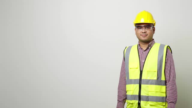 亚洲工人在统一的安全帽安全眼镜指向空白空间的广告文本或模型在工作室孤立的白色背景。4 k决议。视频下载