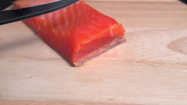 在董事会上，一名男子在鲑鱼的手中切了一把刀。鲜嫩切的红鱼视频素材