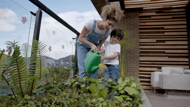 快乐的拉丁美洲母亲教她的儿子如何在他们家的花园浇水视频下载