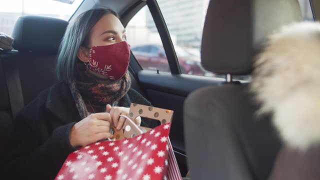 2019冠状病毒病大流行期间，在圣诞购物后开车时佩戴防护口罩的少女视频素材
