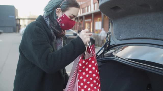 新冠肺炎疫情期间，戴着防护口罩的少女在圣诞购物后将礼物放进车里视频素材