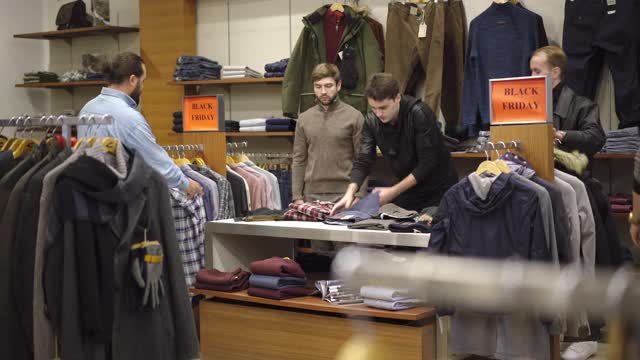 在黑色星期五的大减价期间，白人男人和女人在商店里争抢衣服。男女顾客争先恐后地以最优惠的价格购买商品。时尚和生活方式。视频下载