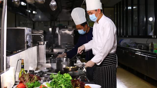 两位亚洲厨师烹饪火焰风格。他在平底锅里用明火煮菜。他在一家餐馆的厨房工作视频素材