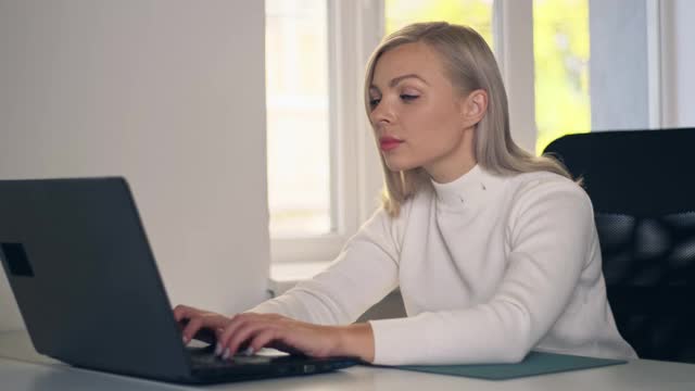 自信的女商人坐在她的办公桌上，在家庭办公室里用笔记本电脑工作。漂亮时髦的女人打字在笔记本电脑的工作。视频下载
