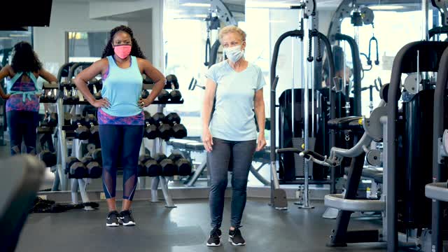 两个女人在健身房做弓步，戴着口罩。视频素材