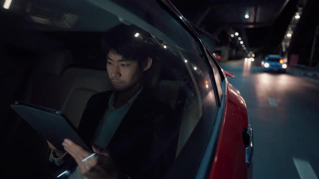 疲惫的商人在回家的路上在车里用平板电脑玩社交媒体视频下载
