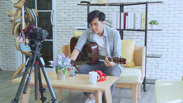 年轻的亚洲男子博客录制视频，影响者现场播放吉他和音乐在社交媒体工作室，在线教程学习视频下载