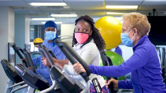 人们在健身房里戴着口罩在椭圆机上锻炼视频素材