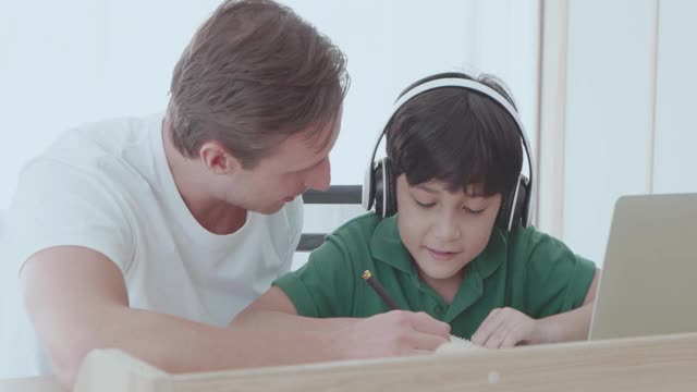 父亲一边用笔记本电脑工作一边帮儿子做作业。视频素材