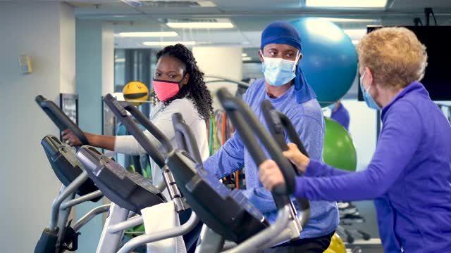 人们在健身房里戴着口罩在椭圆机上锻炼视频素材