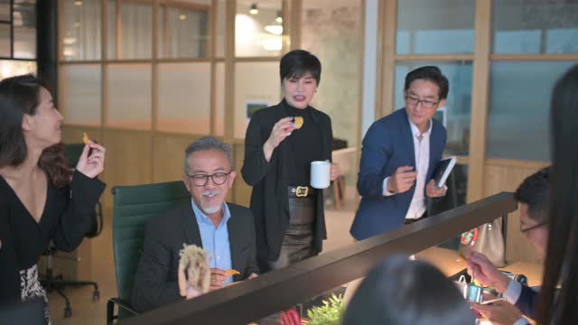 一群亚洲华人白领在工作到很晚的时候休息，并在工作地点的办公室吃零食视频下载