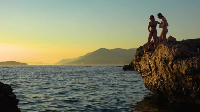日落时分，克罗地亚海岸的青少年们从悬崖上跳下，游回杜布罗夫尼克附近的海岸视频下载