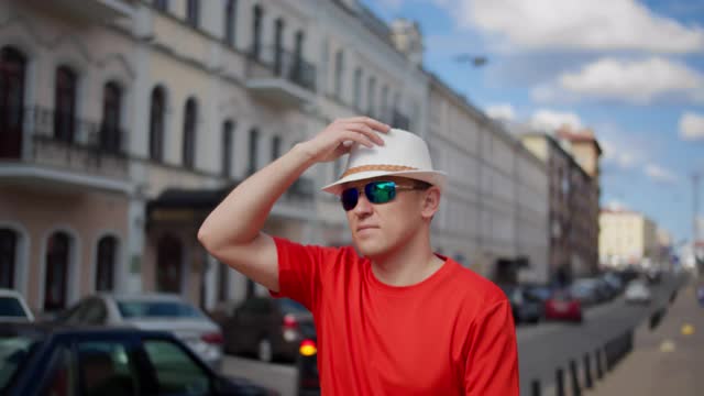 一个戴着帽子的游客走在城市的街道上，检查周围的环境，摄像机的移动视频下载