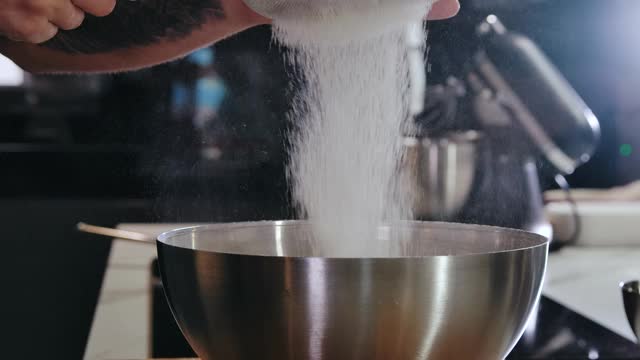 厨师正在用筛子筛面粉，然后在金属碗里搅拌配料。概念，烹饪，烘焙和糖果。在厨房里准备面粉来烤面包视频素材