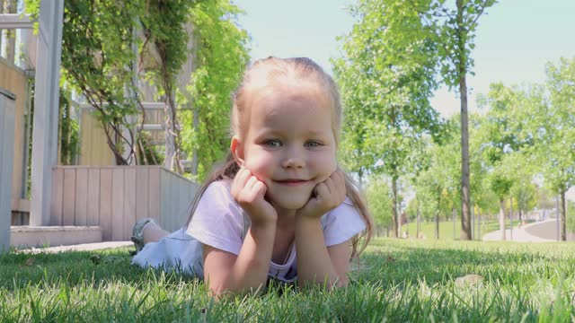 特写镜头微笑的小可爱的小女孩躺在绿草地上。一个漂亮的小女孩对着镜头微笑。童年视频素材