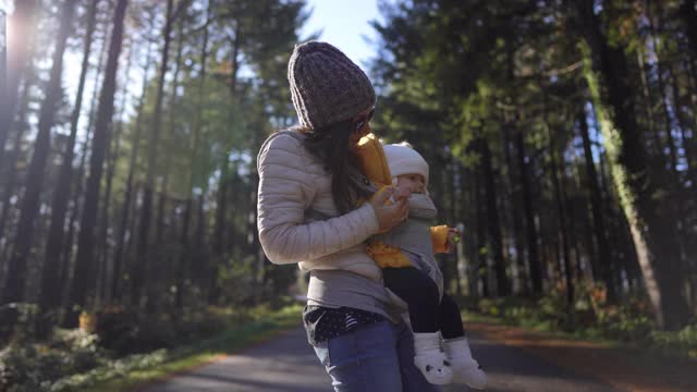 年轻的母亲抱着她的婴儿在婴儿车和她玩，而站在道路上的自然视频素材