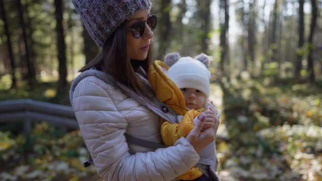 一位年轻的母亲背着她的婴儿在一个阳光明媚的日子里穿过森林视频素材