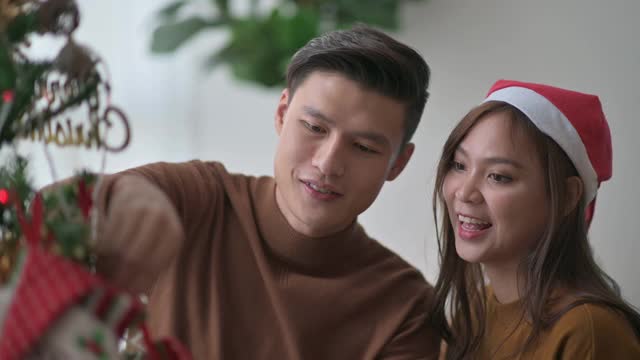 亚洲华人年轻夫妇在家里的客厅装饰圣诞树庆祝圣诞节视频下载